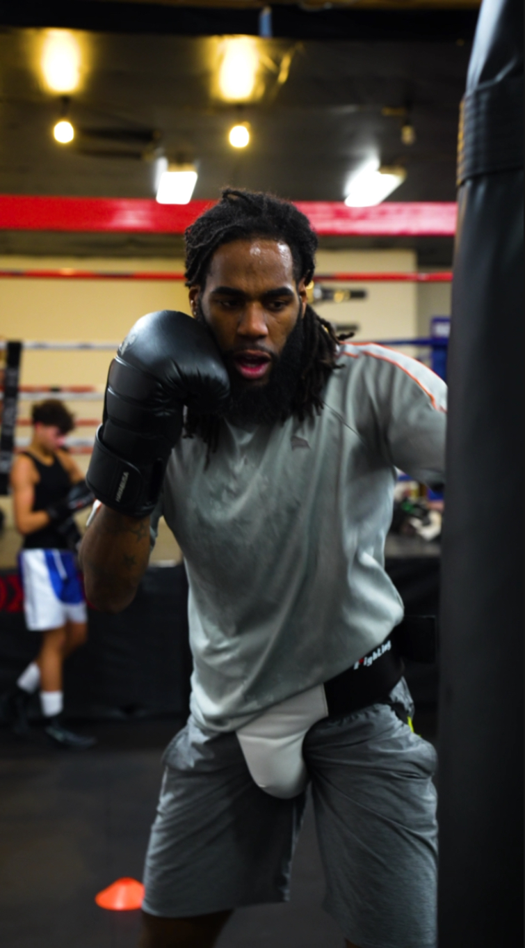 Jayy Klipsz working the heavy bag in the gym with another athlete training behind him