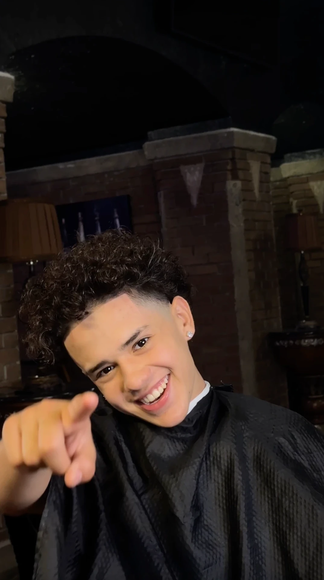 Client smiling and pointing at the camera after a curly top taper in the barber chair