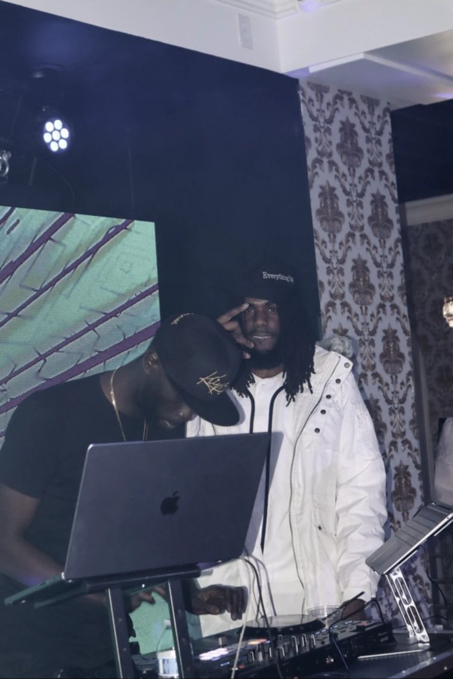 Cubano Jayy in a white hooded jacket behind DJ equipment under stage lighting