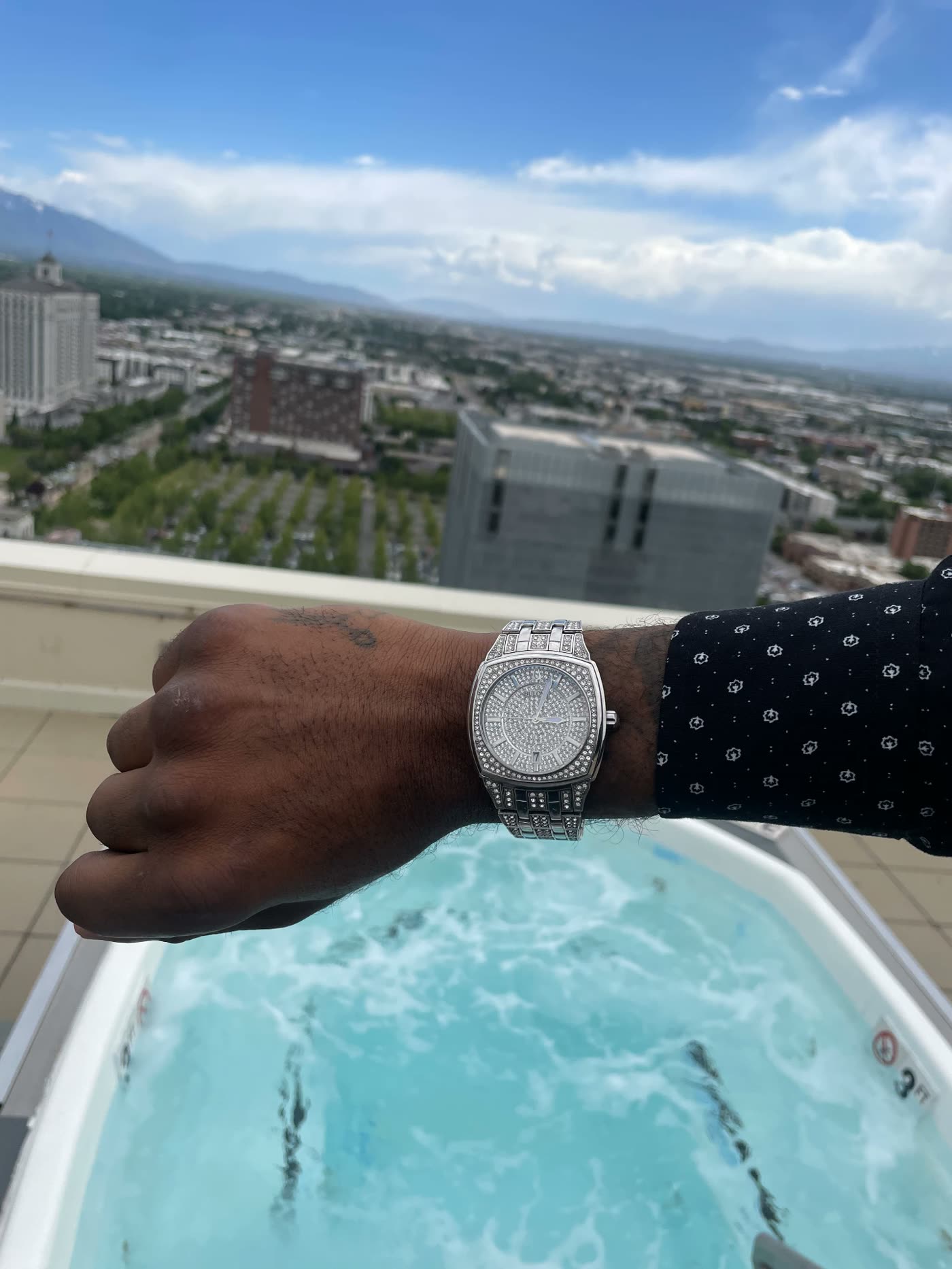Jayy Klipsz wearing a silver watch with a wide city and mountain view behind him