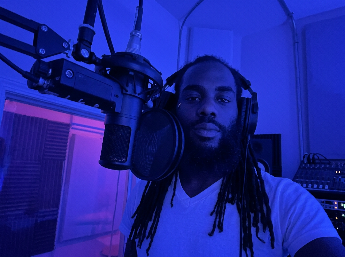 Cubano Jayy in a blue-lit studio booth with a microphone and headphones