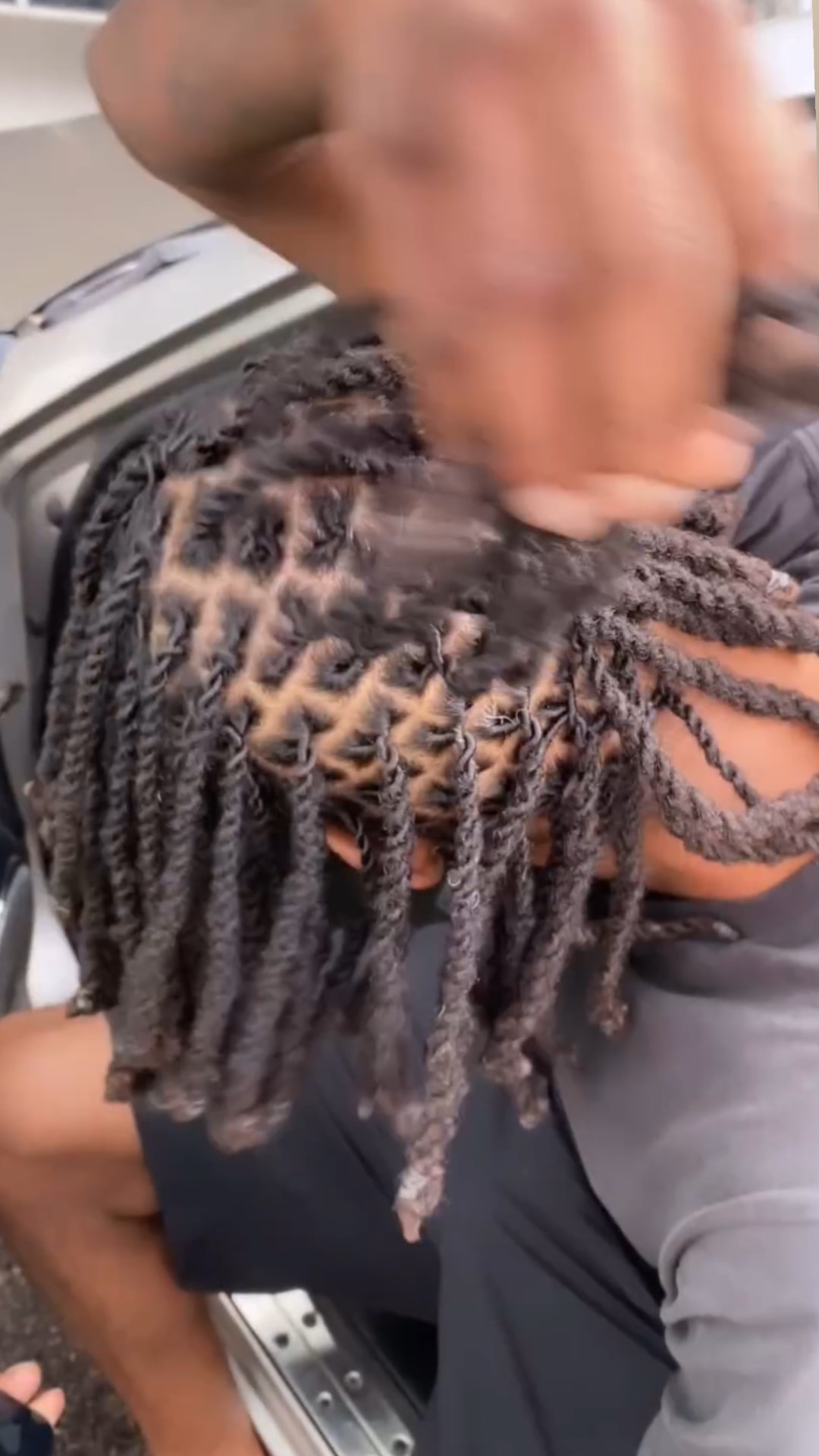 Overhead view of freshly retwisted locs with a uniform diamond parting grid, hands working through the sections