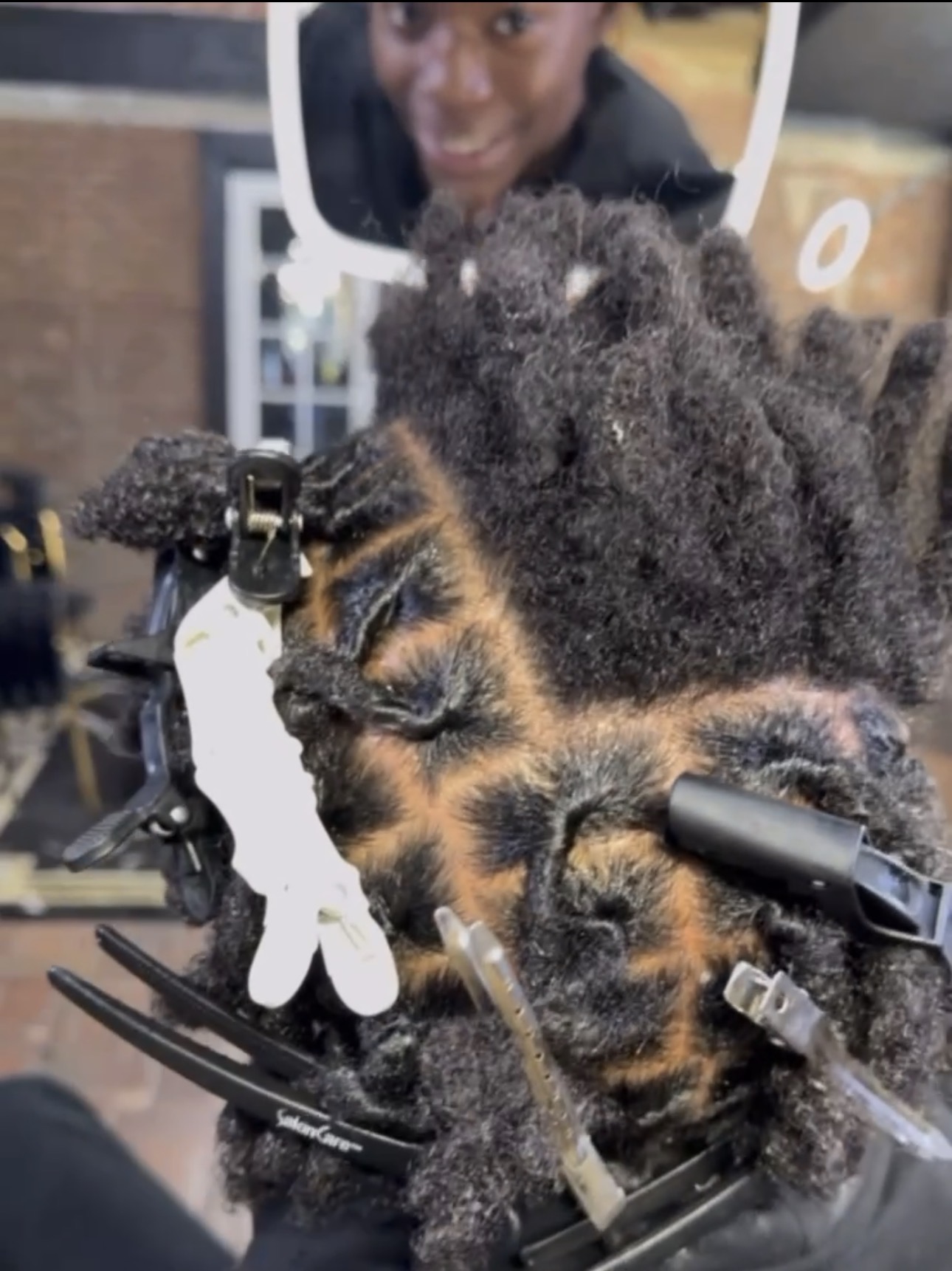 Close detail of crochet work in progress on dense locs, sectioning clips holding the surrounding hair